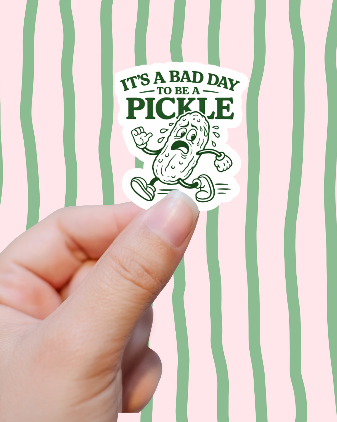 Sticker with pickle graphic and text held against a pink background with green stripes